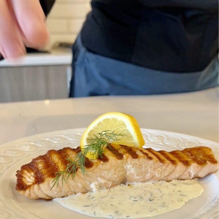 Grilled salmon fillet with lemon wedge and creamy sauce on a white plate.